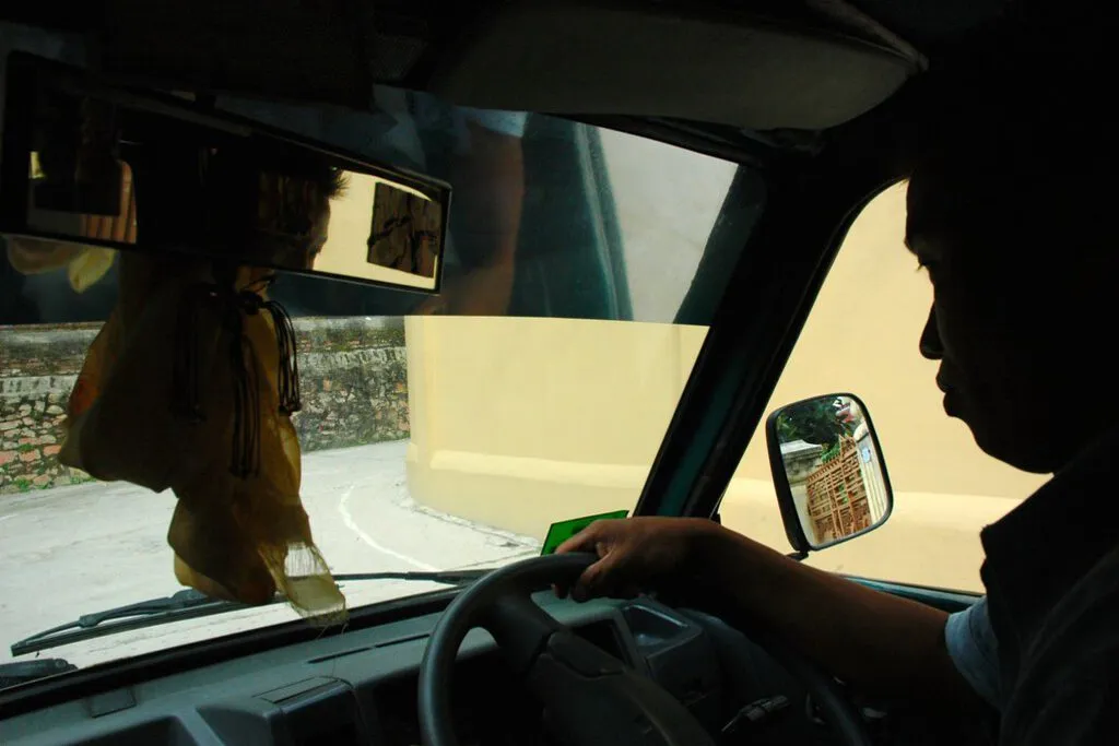 A driver at the wheel of his car in Bali, morning light filling the windscreen