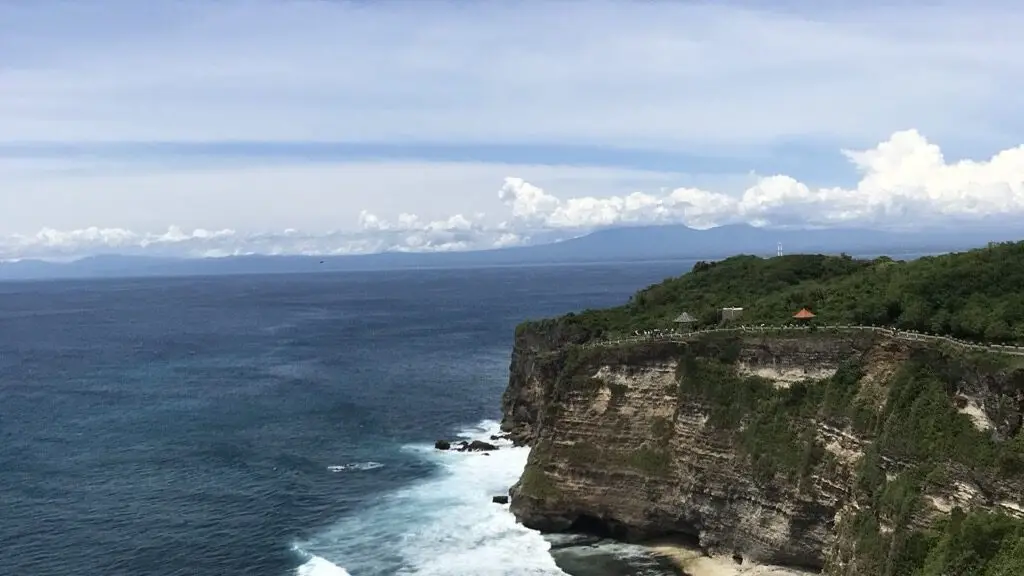 A Bali clifftop above deep blue sea, with white surf breaking against the rocks below on a clear bright morning