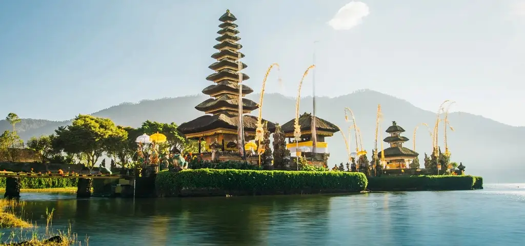 A tiered Balinese temple at the edge of a mountain lake, reflected in still water