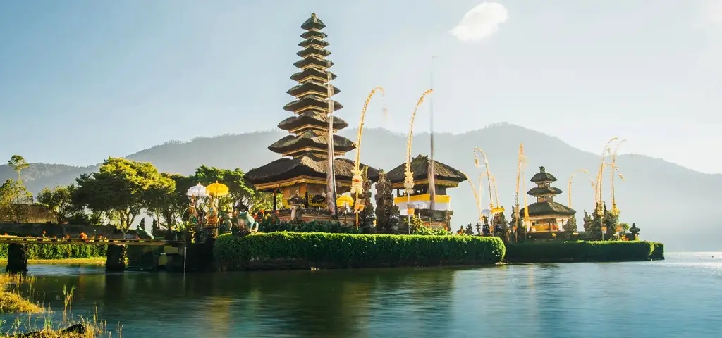 A tiered Balinese temple at the edge of a mountain lake, reflected in still water
