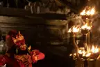 A Kecak performer in a red costume and gold headdress beside a torch stand of open flames in a stone courtyard at night