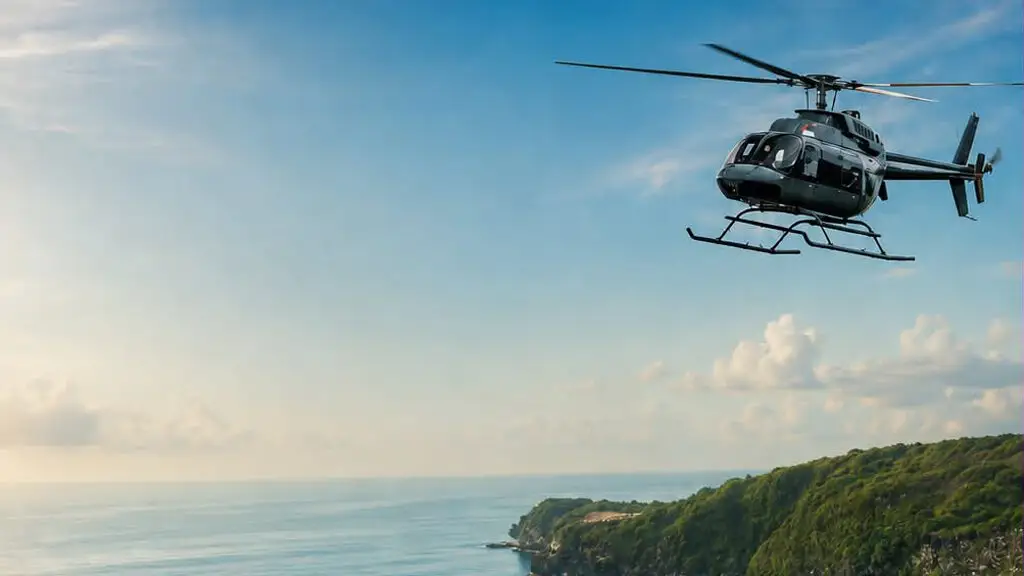 A dark helicopter flying over a calm blue sea towards a green forested headland under a pale sky