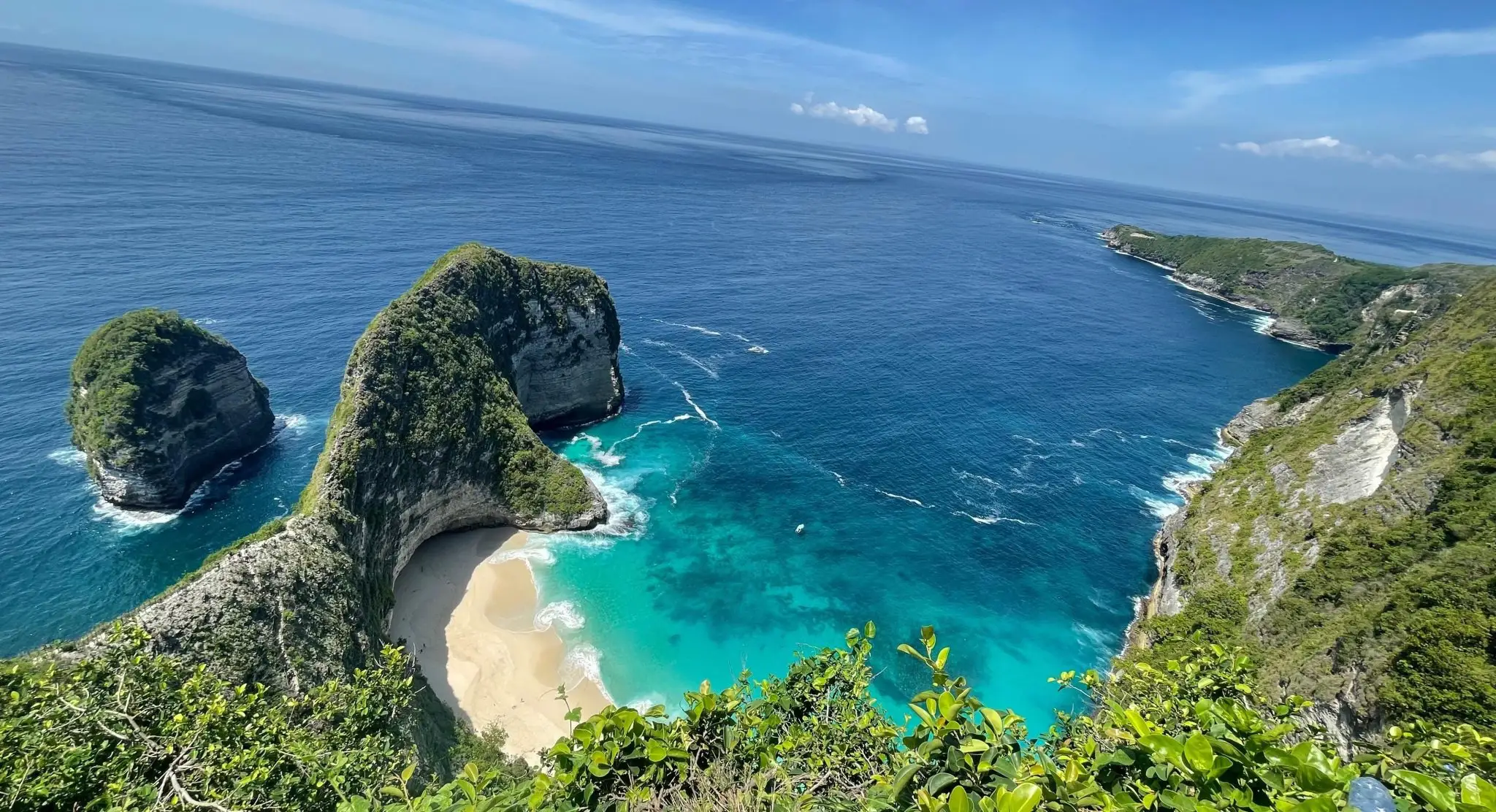 Kelingking Beach on Nusa Penida seen from the clifftop, a green headland above white sand and turquoise sea under a clear sky