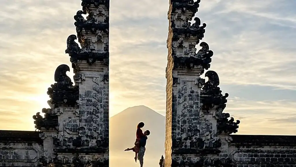 A couple silhouetted between the two carved stone halves of the Lempuyang split gate, with Mount Agung behind and their reflection below