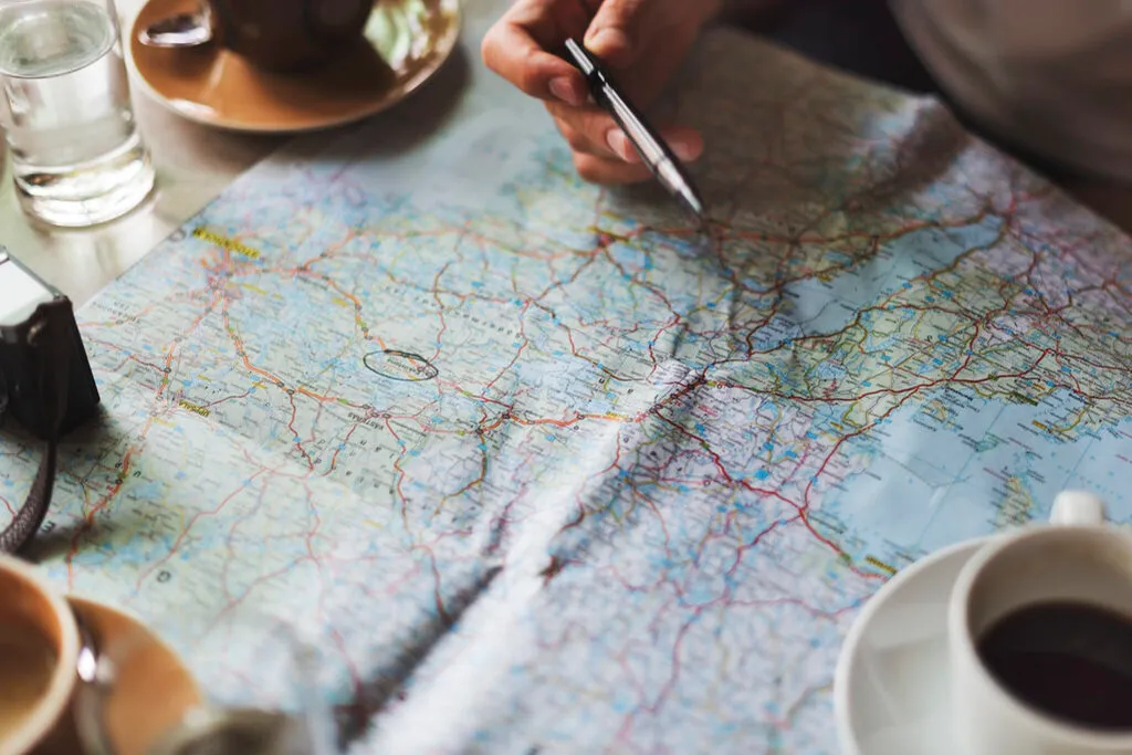 A hand tracing a route across an open paper map beside a cup of coffee